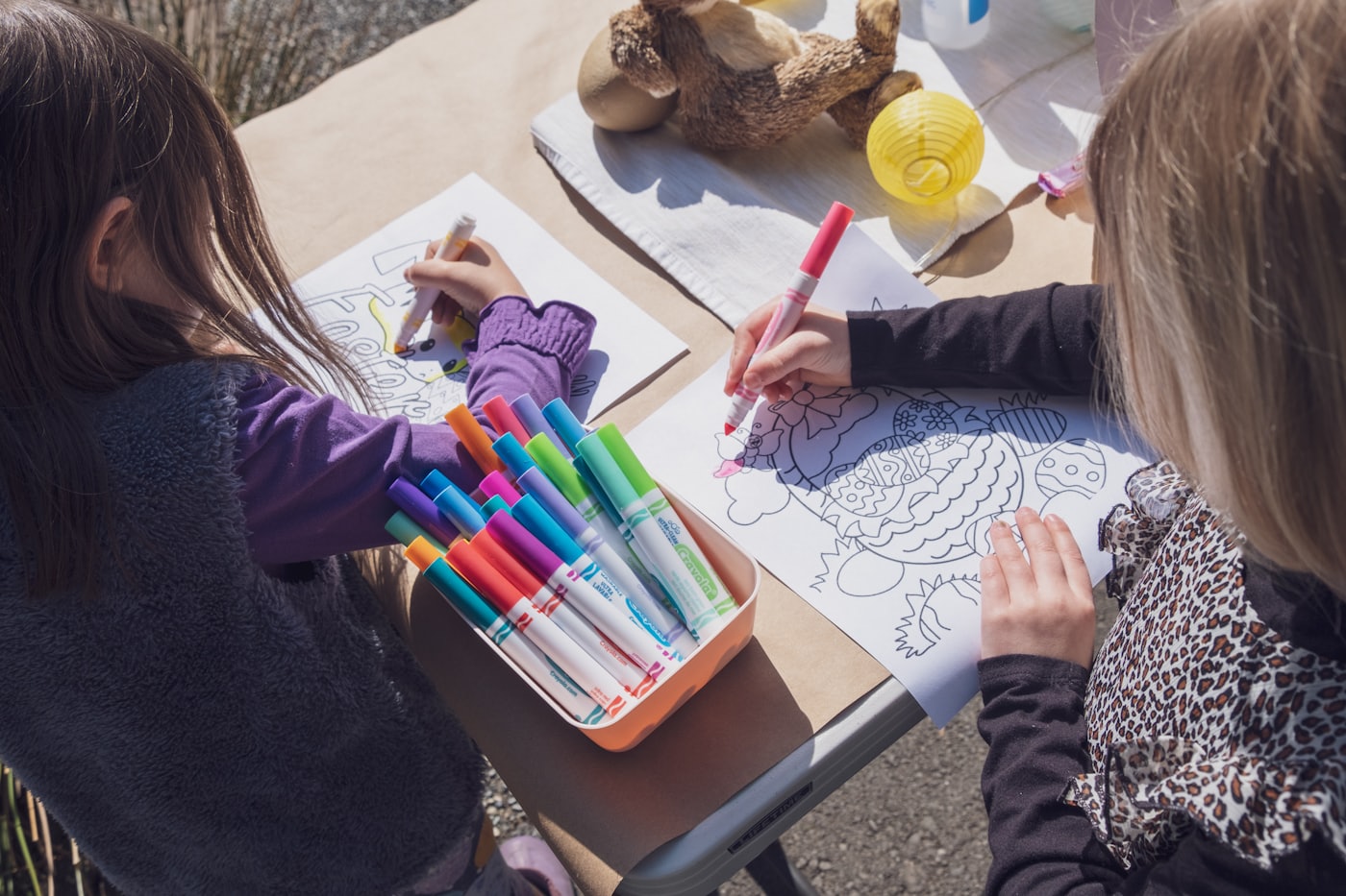 Two kids coloring printable activity sheets at a craft table with crayons and markers